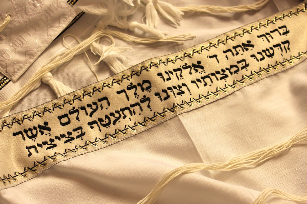 Nahaufnahme eines weißen jüdischen Gebetsschals (Takit) mit goldener Atarah (Halsband). Auf dem goldenen Band ist der traditionelle hebräische Segen zum Anlegen des Tallit eingestickt, umrahmz von kustvollen Mustern.