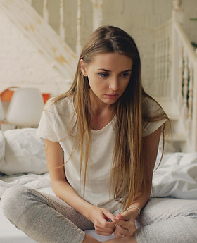 Depressed young woman sitting in bed and