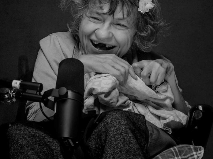 An older, Canadian woman in a wheelchair laughs into a microphone.
