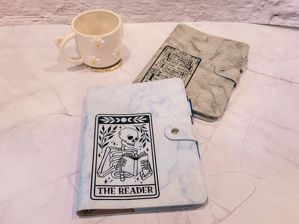 Two marble-patterned journals, one labeled "The Reader" with a skeleton design, and a daisy-patterned mug on a marble surface.