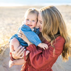 Mother holding smiling baby girl on beach at sunset, natural lifestyle portrait by family photographer in Los Angeles