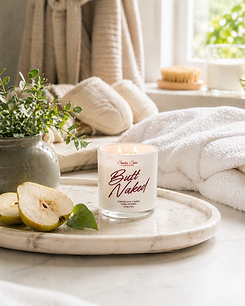 Butt Naked soy candle in white glass jar on marble tray beside pear slices, towels, and greenery