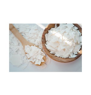 Soy wax flakes in brown bowl near wooden spoon with soy flakes.