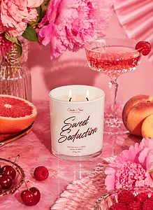 Sweet Seduction soy candle with pink florals, citrus, berries, and pink cocktail in feminine tabletop setting