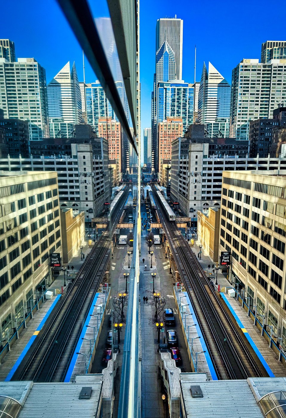 Through the Looking Glass: Symmetry in Motion Chicago elevated tracks and skyscrapers mirrored along a sharp central building reflection.