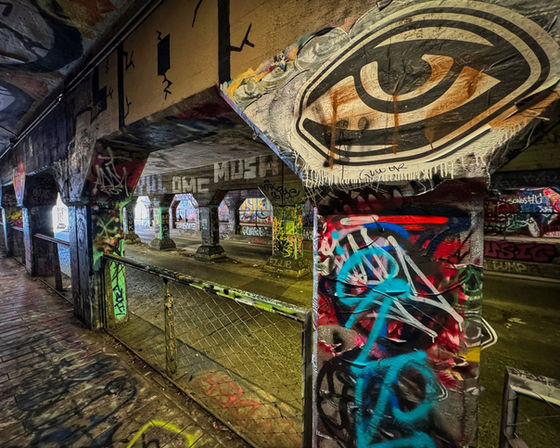 Graffiti-covered riverside passage beneath a large painted eye.