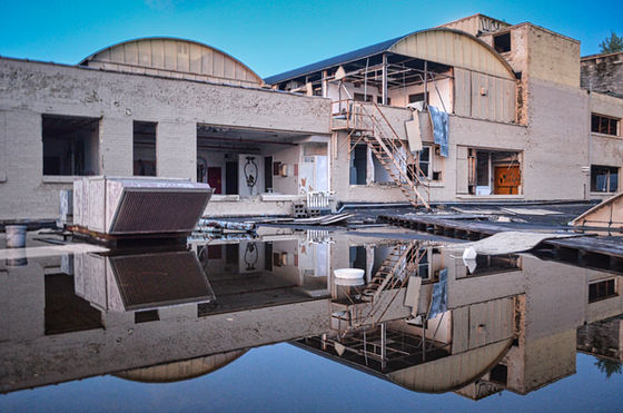 Partly dismantled industrial building and curved rooflines reflected in still water.