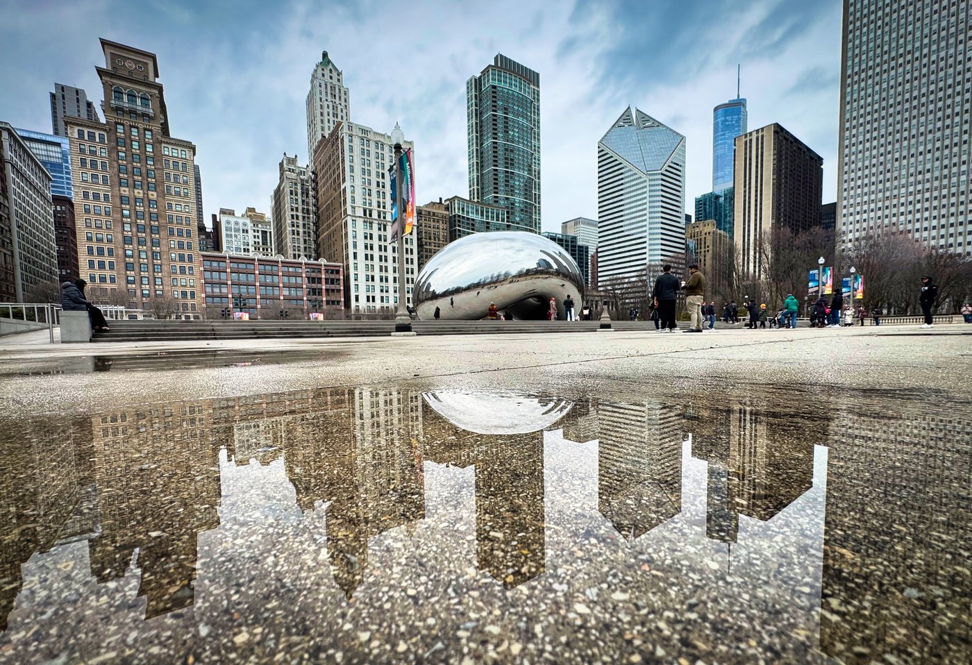 Concrete Canvas: Chicago Reflected City towers and a mirrored sculpture reflected in a shallow plaza puddle.