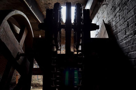 Dark mechanical wheels and gears silhouetted against a bright opening.