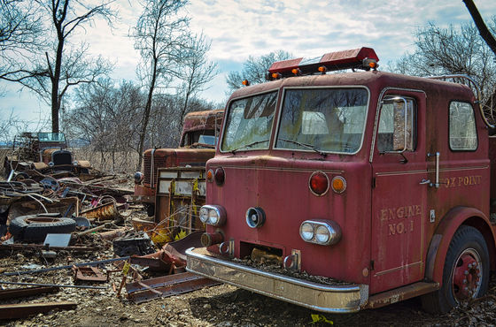 Old red fire engine among scrap and other weathered vehicles.