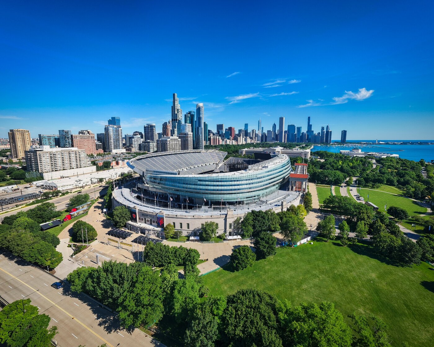 Daylight aerial view of Soldier Field amid green lawns with the Chicago skyline behind.
