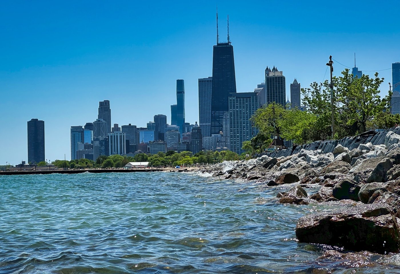 Stones Below the Skyline Rocky Chicago shoreline with lake water and downtown towers beneath clear blue sky.