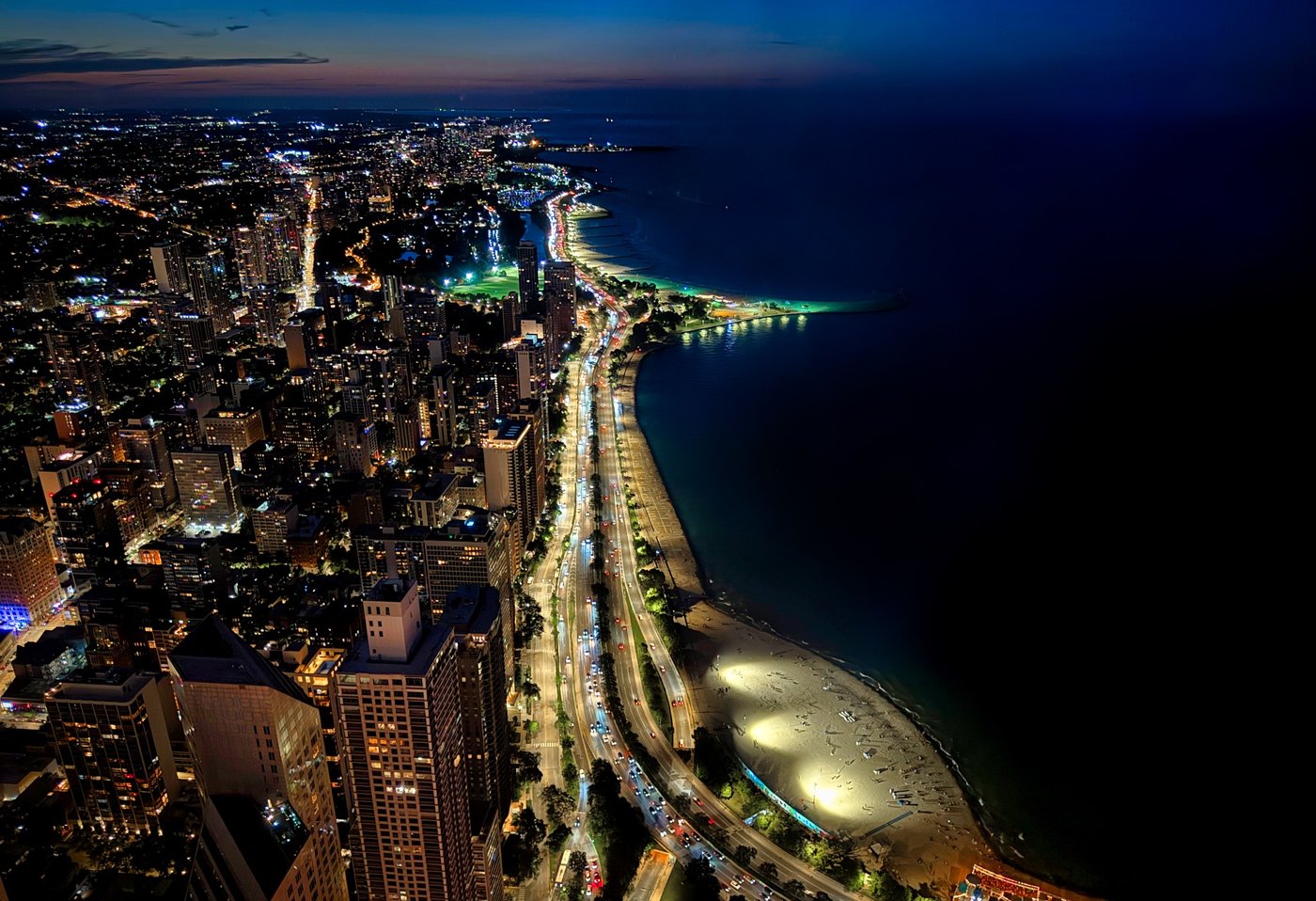 The Luminous Coast Nighttime aerial view of a brightly lit road curving along a dark shoreline.
