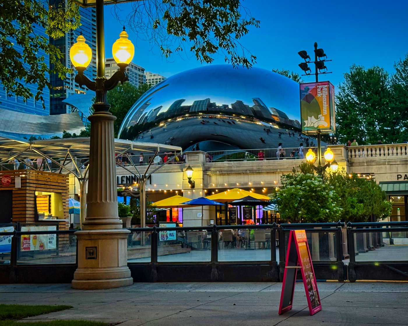 Reflective rounded sculpture above outdoor seating, trees, and lamps in Chicago.
