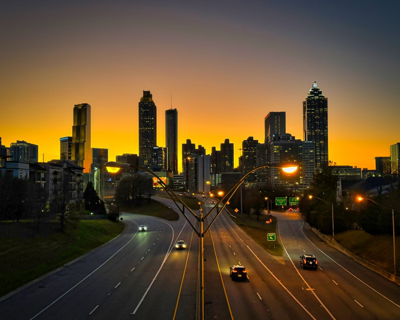 Curving roadway and streetlights leading toward a skyline at sunset.