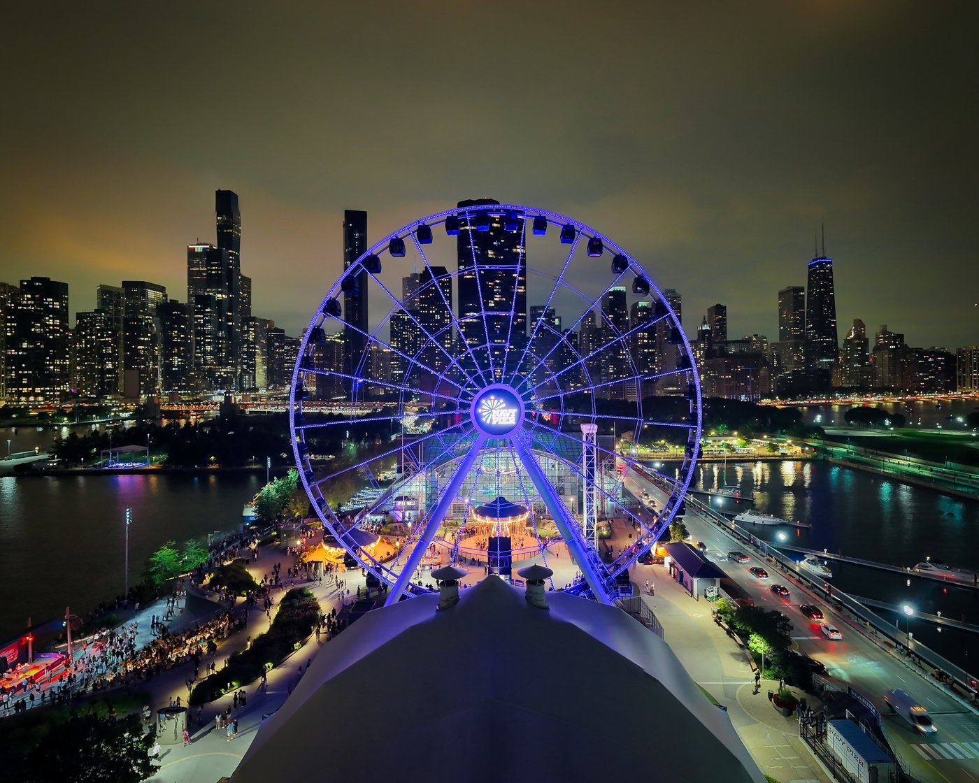 Illuminated Navy Pier Ferris wheel above a pale roof against the Chicago night skyline.