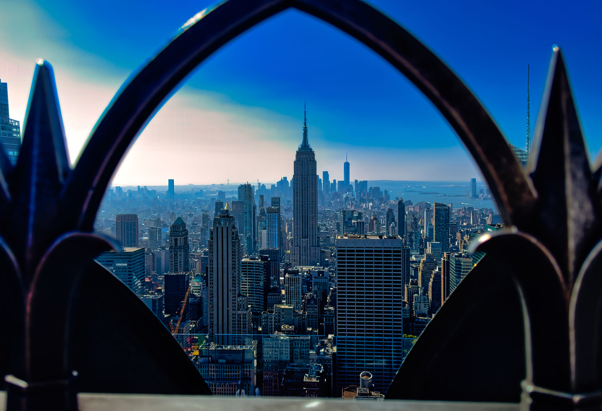 Empire State Building and Manhattan skyline framed by a dark pointed railing opening.