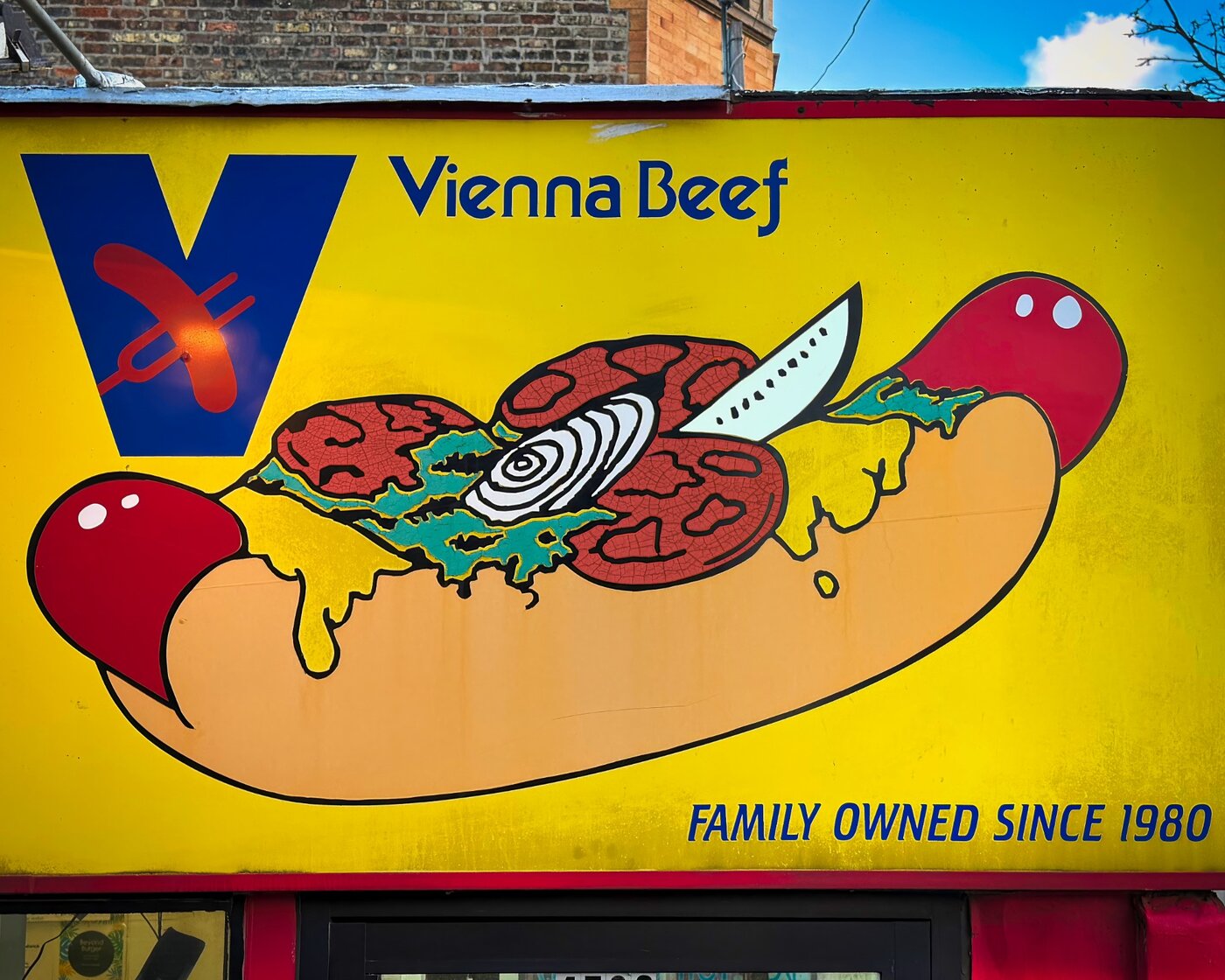 Painted hot dog with toppings on a yellow Vienna Beef sign.