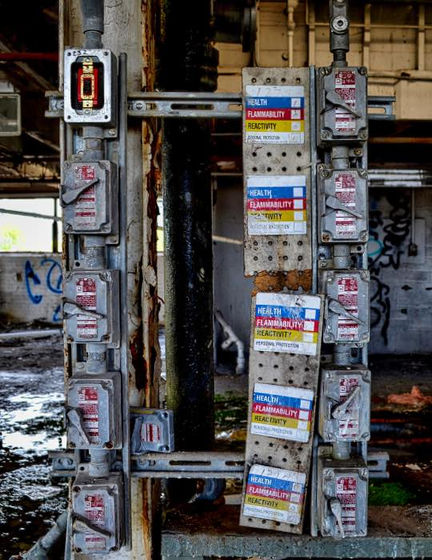 Weathered electrical boxes and hazard labels on corroded industrial supports.