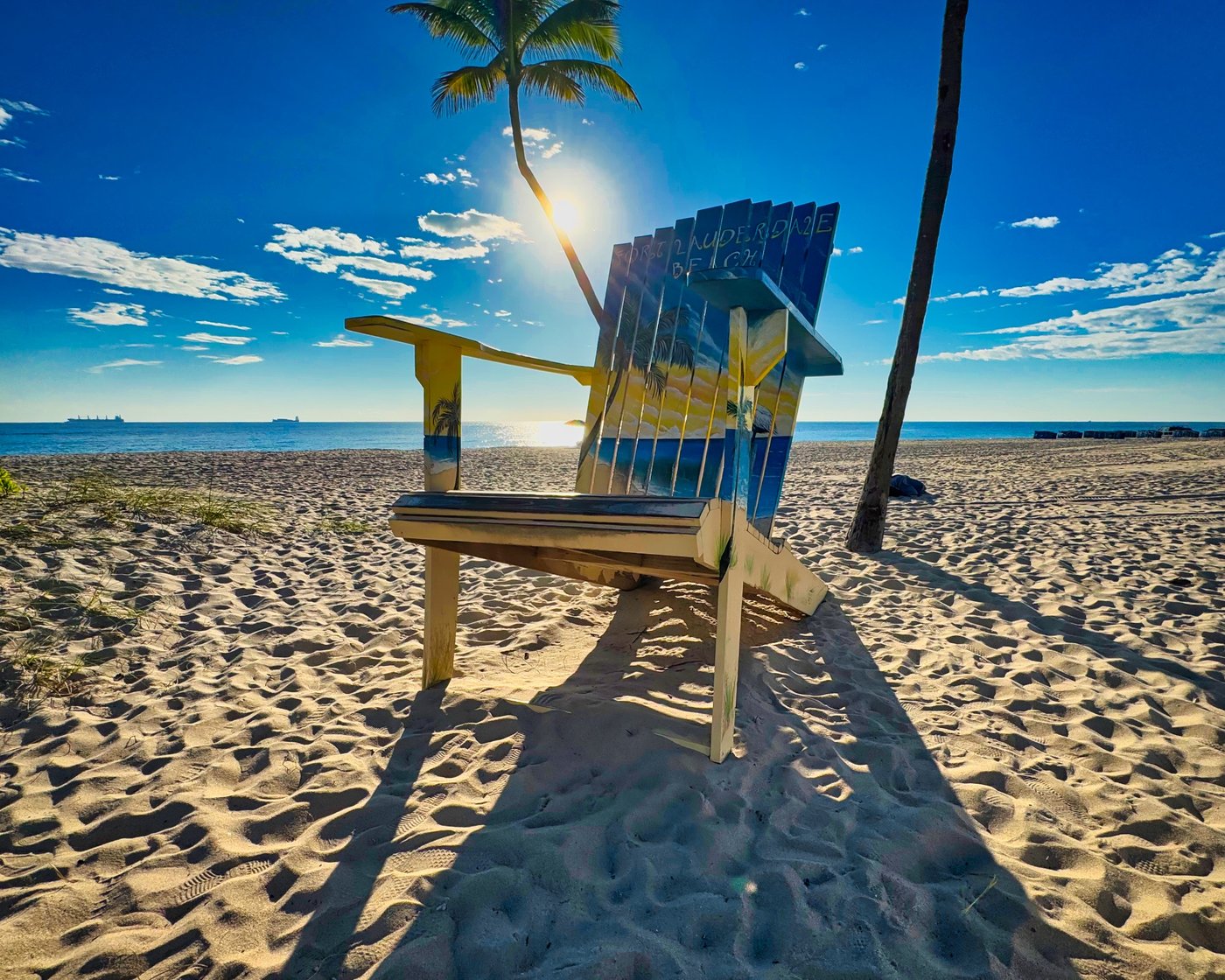 Oversized yellow and blue beach chair between palm trunks.