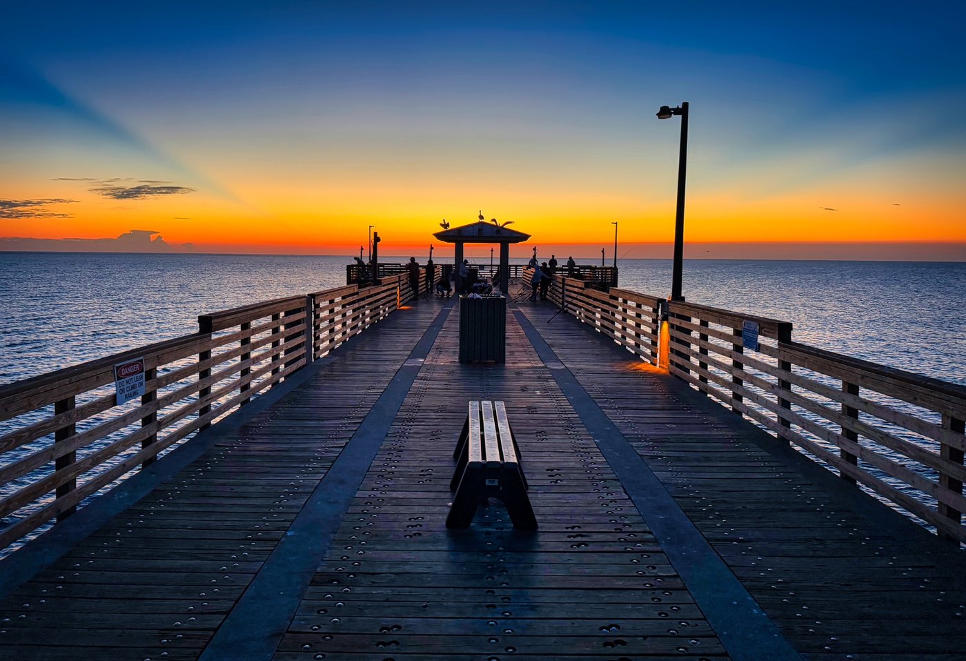 Peace on the Pier Wooden pier and benches leading toward a shelter beneath an orange horizon.