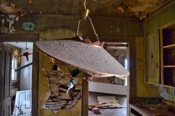 Tilted, dust-covered hanging light shade inside a deteriorating room.