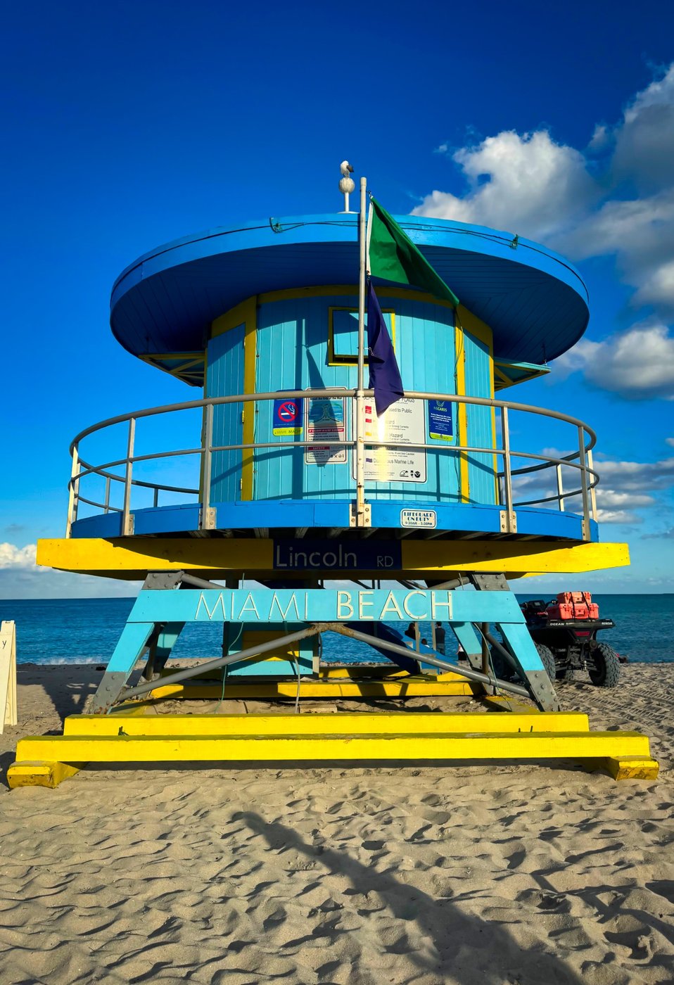Vibrance on the Beach 4 Round blue lifeguard tower with yellow supports and flags beside the ocean.