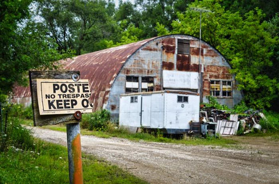 No-trespassing sign before a weathered building with a rounded metal roof.