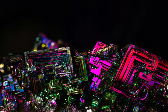 Metallic stepped crystals reflecting pink, green, and gold against black.