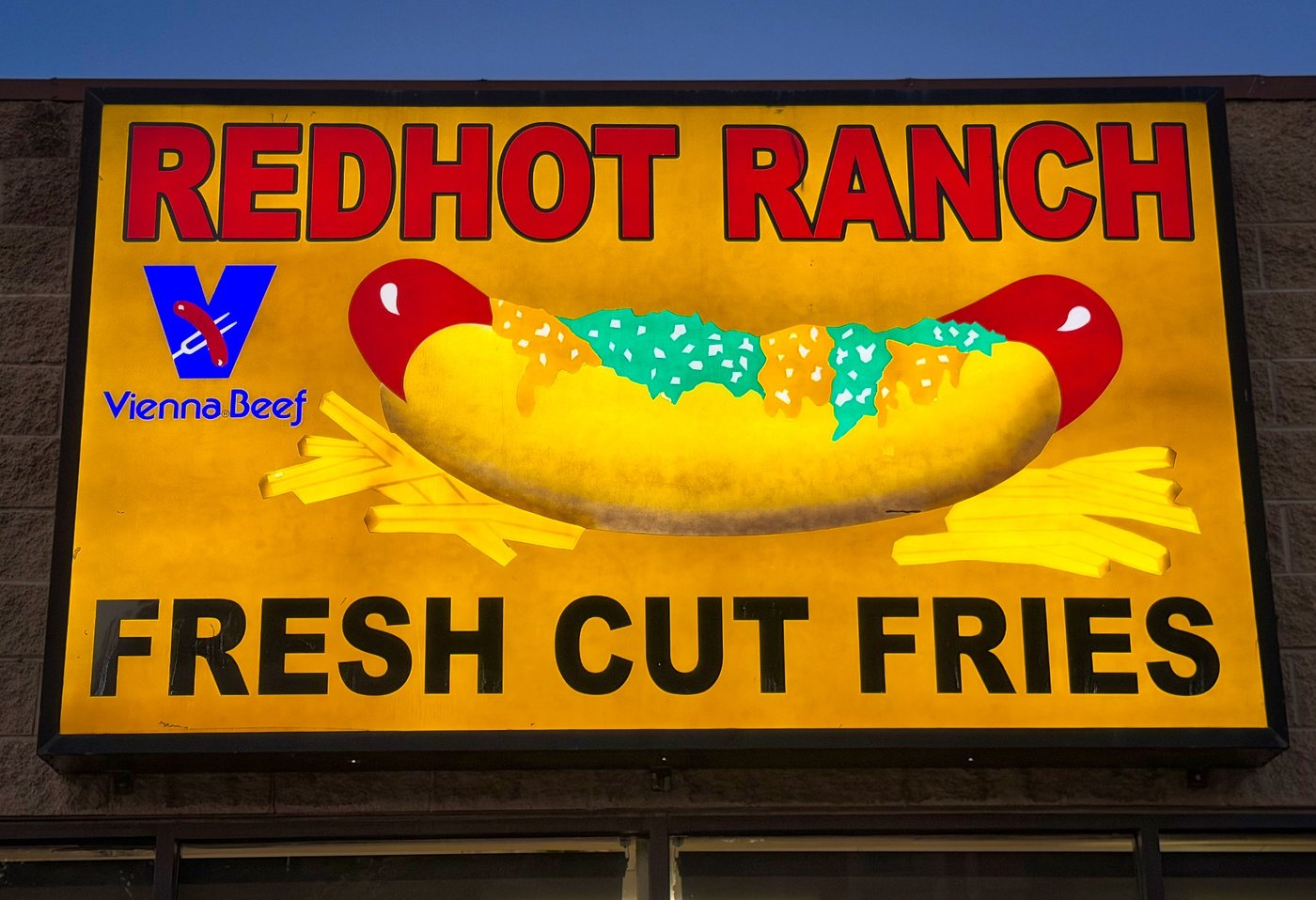 Redhot Ranch Illuminated Redhot Ranch sign advertising hot dogs and fresh cut fries against a dark background.