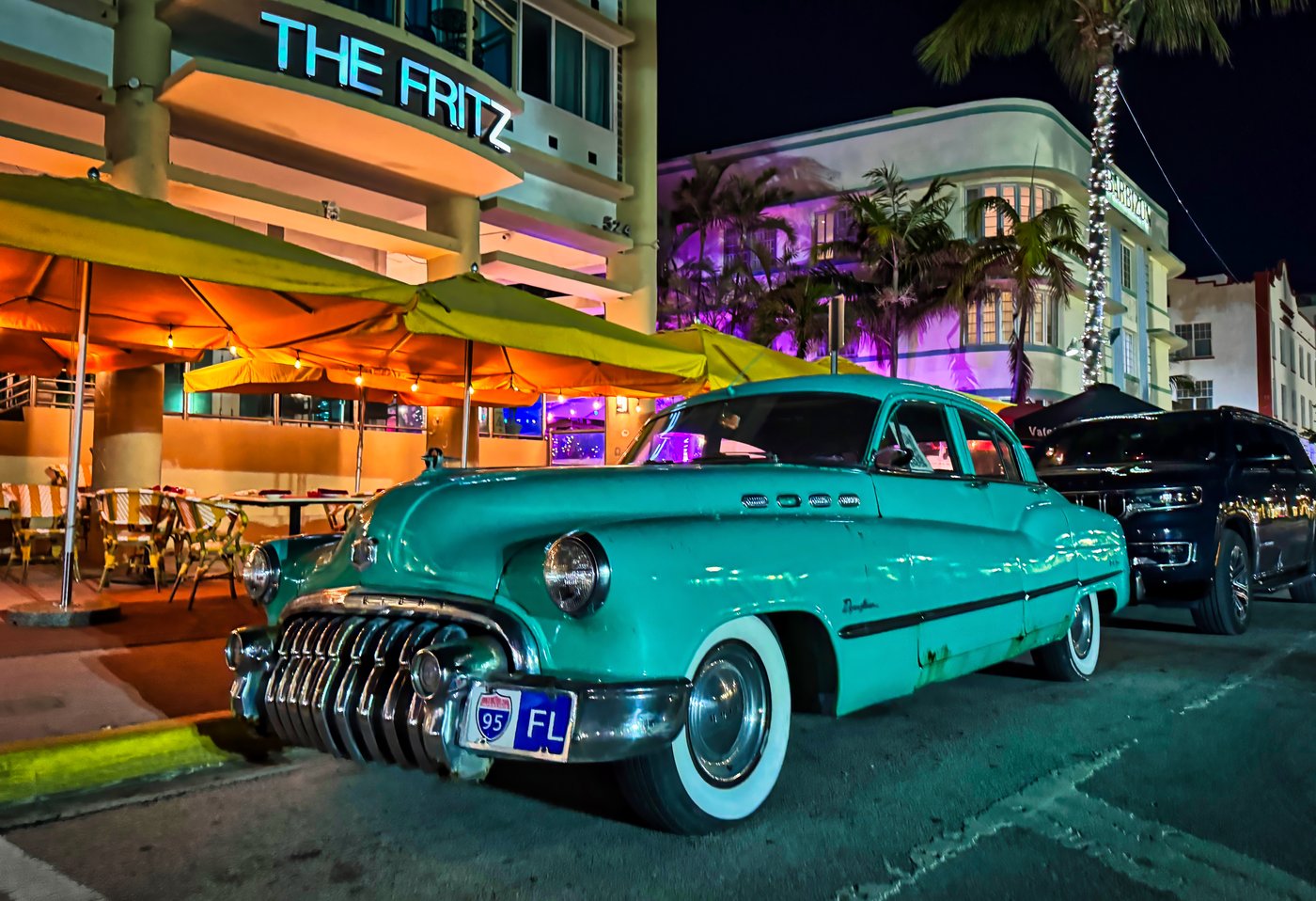 South Beach Classic Turquoise vintage car beneath orange restaurant awnings at night.