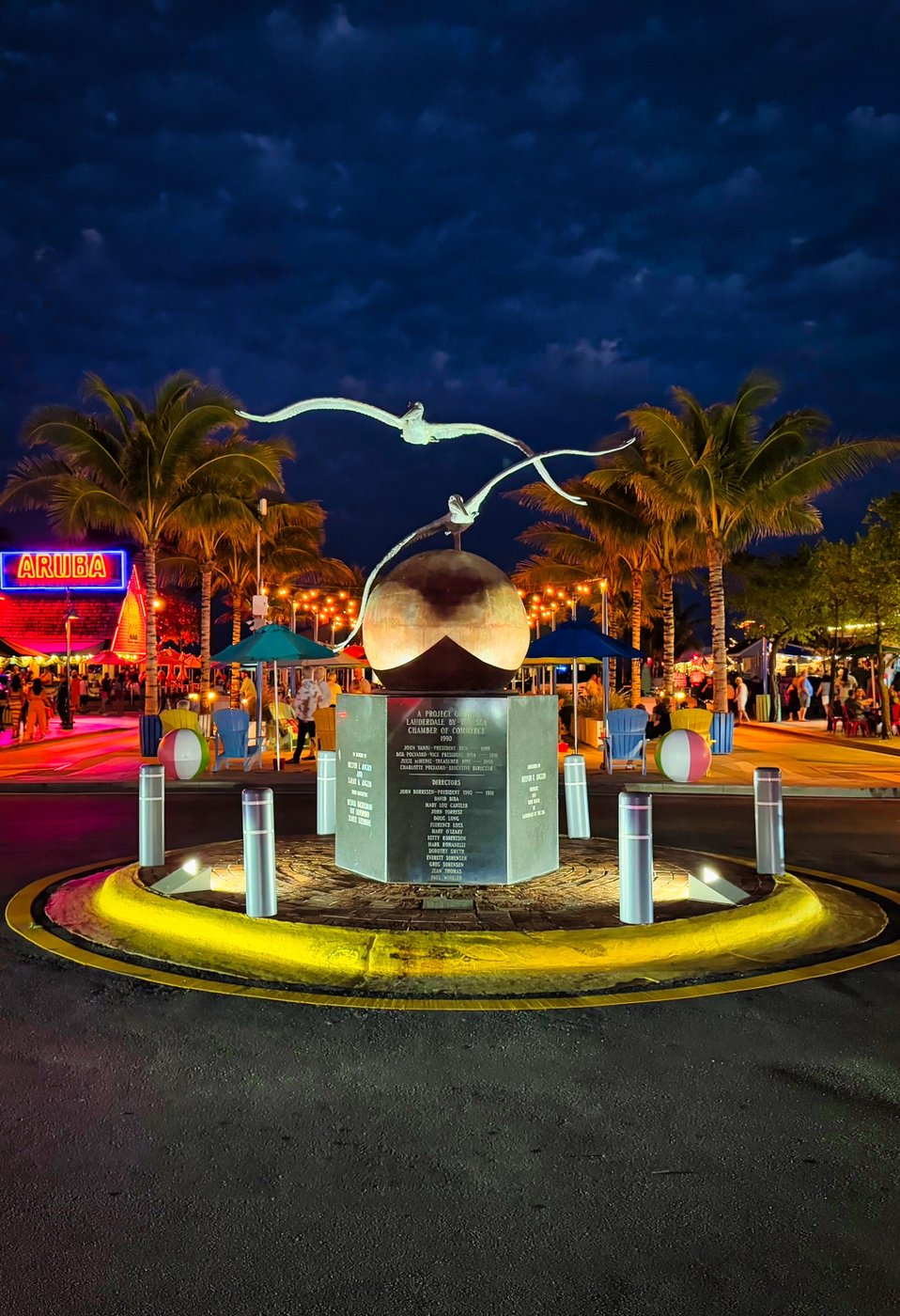 Lauderdale-by-the-Sea Beacon Illuminated roundabout monument with bird forms, palms, and a yellow curb.