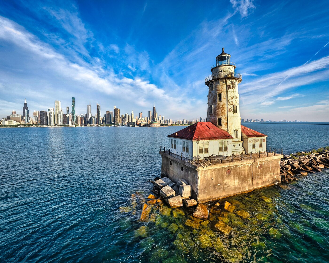 Stone lighthouse with a red roof on a rocky breakwater against the Chicago skyline.