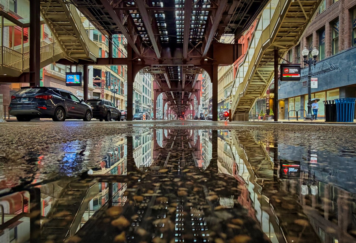 Rails in the Rain Elevated railway beams and nearby buildings reflected in a puddle on rough Chicago pavement.