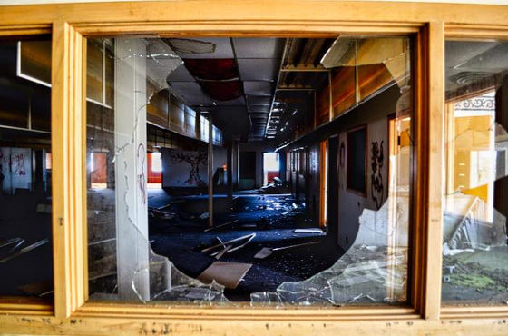 Broken interior window framing a long, dark corridor.