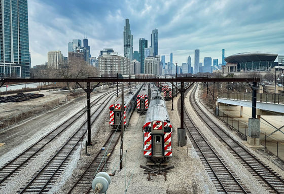 Commuter trains on parallel tracks leading toward Chicago's skyline under gray clouds.