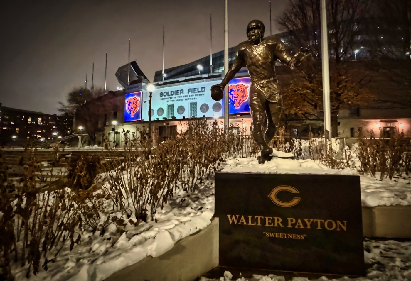 A Legend in Winter Walter Payton statue outside Soldier Field surrounded by snow at night.