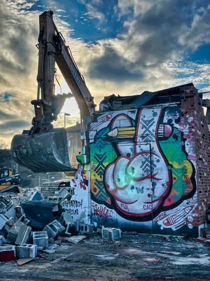 Excavator beside a graffiti-covered wall and demolition rubble.