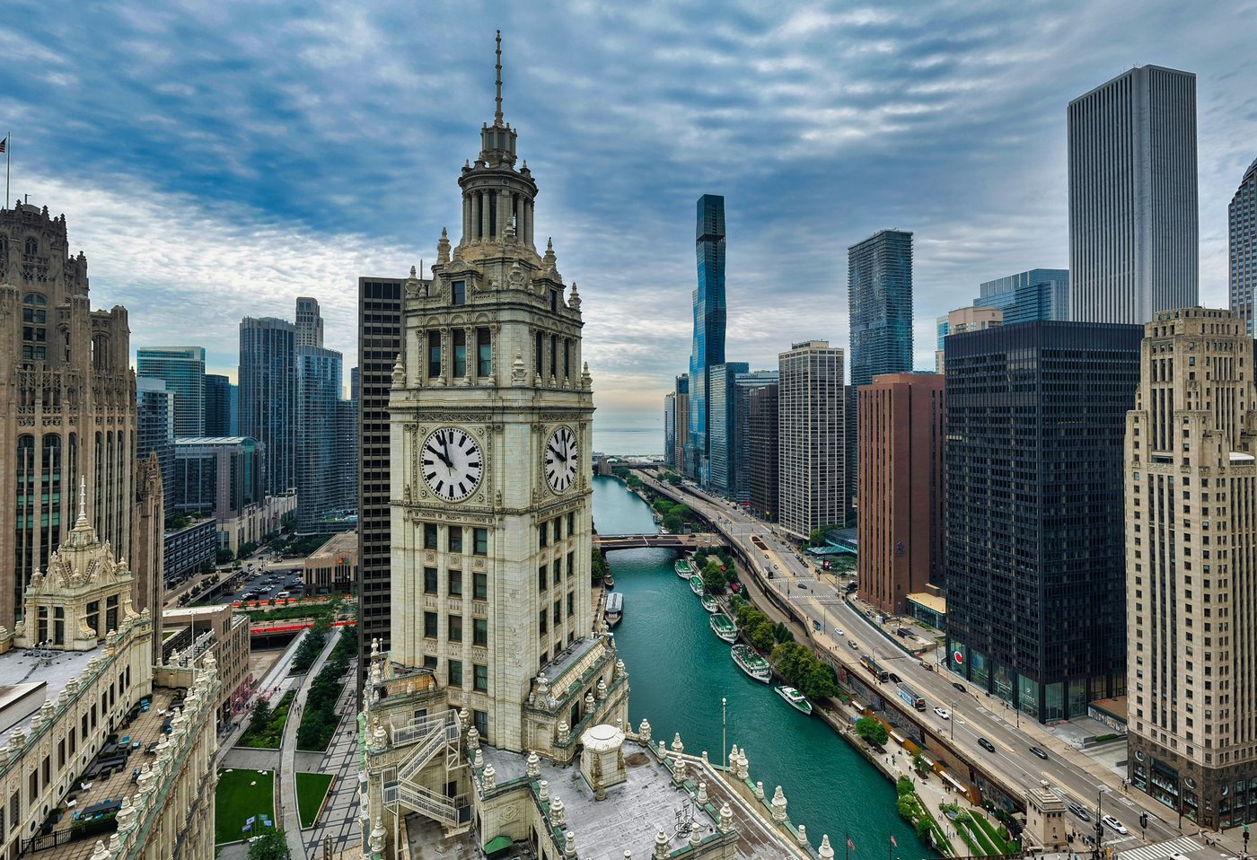 The River Keeps Time Clock tower beside the Chicago River with bridges and skyscrapers under patterned clouds.
