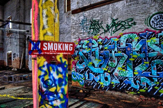 No-smoking sign on a painted column in a graffiti-covered interior.