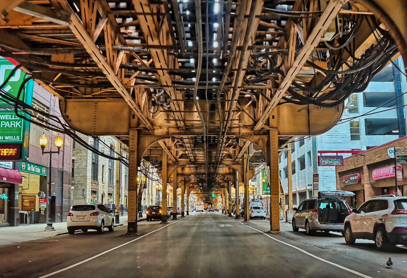 Under the Long Span Chicago street under repeating elevated railway beams and bundled cables in daylight.