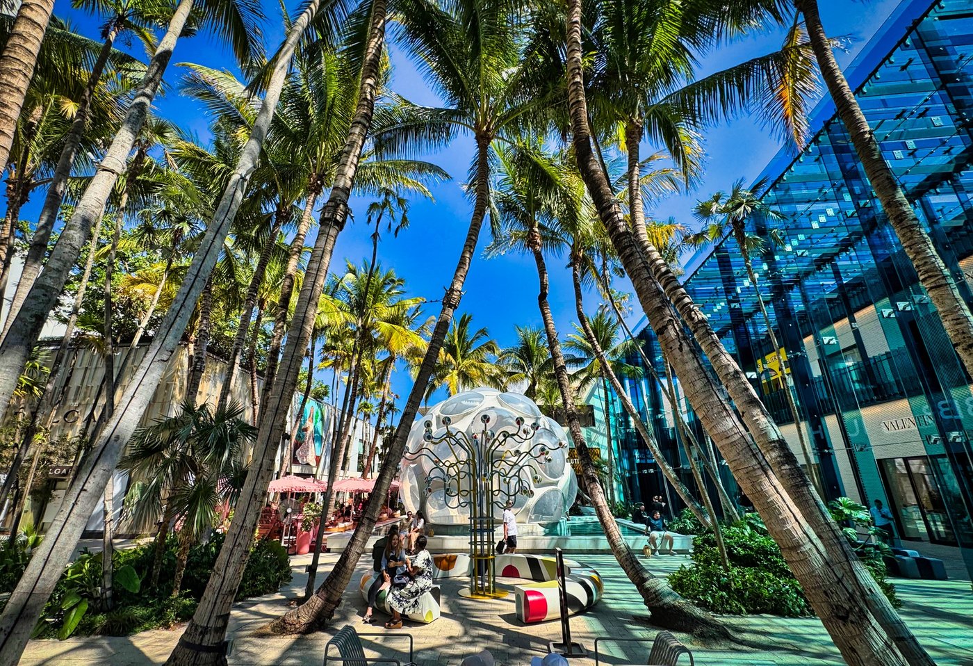 Modern Palm Oasis Palm-filled courtyard beside a reflective blue building and pale rounded sculpture.