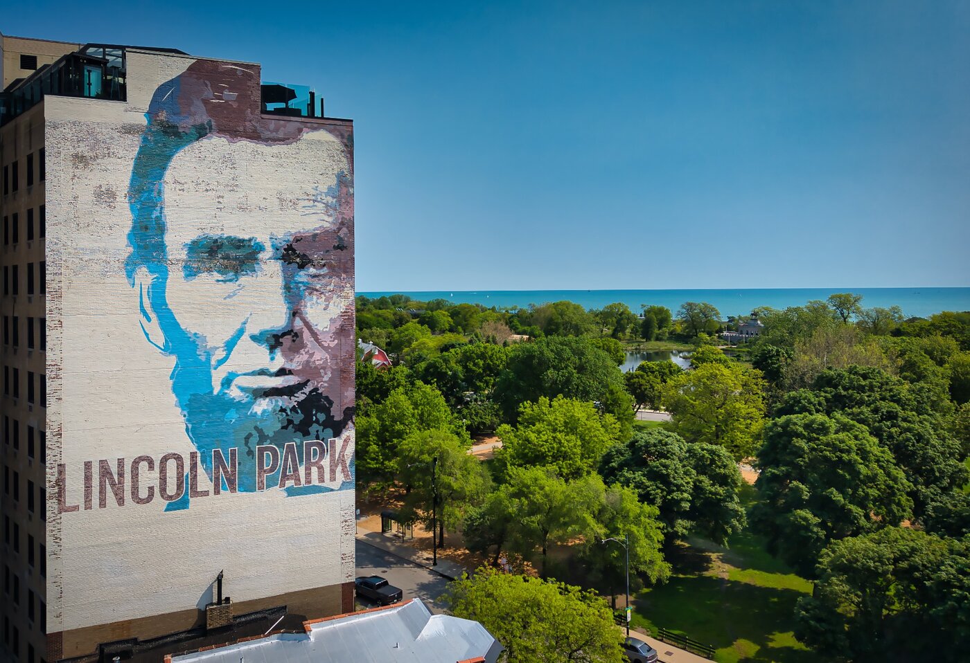Portrait Above the Canopy Large portrait mural beside a green park and distant blue water.