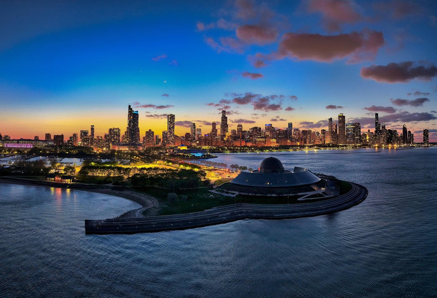 The Lake's Last Light Chicago skyline at dusk across a curved shoreline and low domed waterfront building.