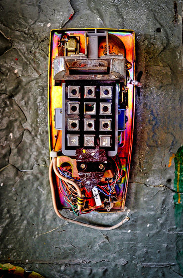 Damaged keypad telephone with exposed wiring on a rough gray wall.