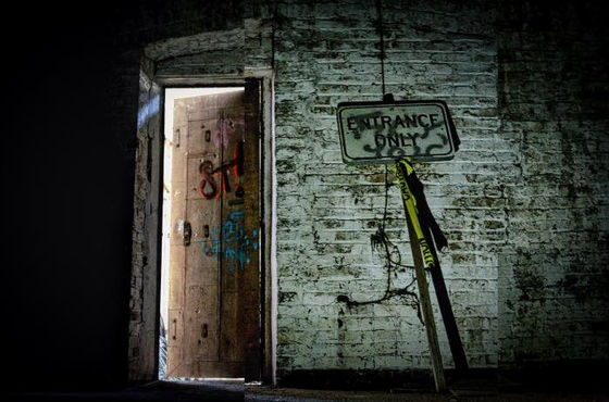 Open doorway and tilted entrance-only sign in a dark brick interior.