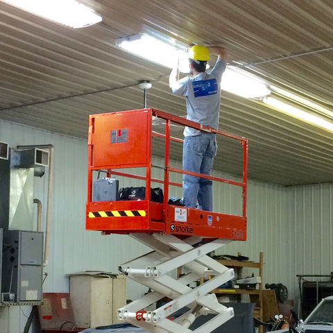 Electrician in yellow helmet fixes lights from scissor lift in warehouse