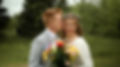 Joyful bride and groom share a playful kiss during an outdoor wedding, holding a vibrant bouquet, captured by a candid weddin
