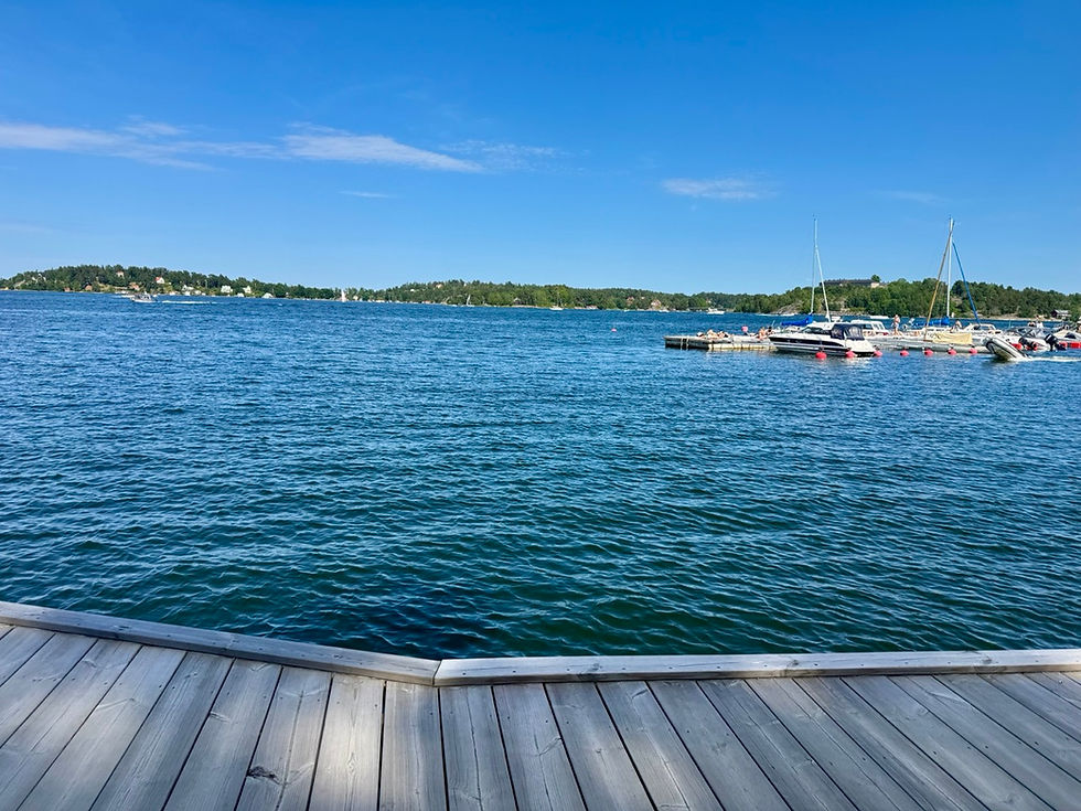 Wooden dock over blue harbor water with sailboats at a small marina under a clear sky