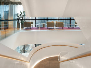 Modern interior featuring a curved white staircase finished in Marmorino Antico 300 lime plaster, with timber handrails, glass balustrades, and a lounge seating area overlooking the city through floor-to-ceiling windows.